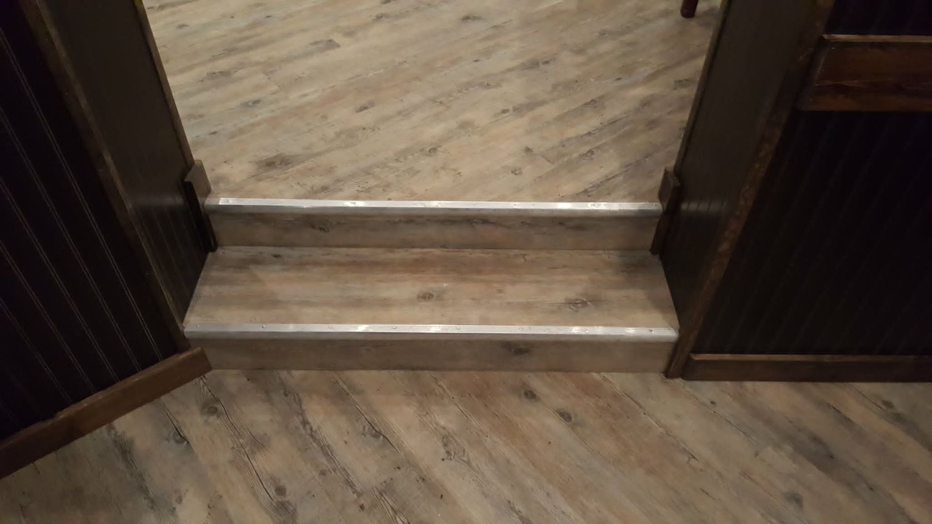 Wooden floor with a small step up between two dark-paneled doorway openings.