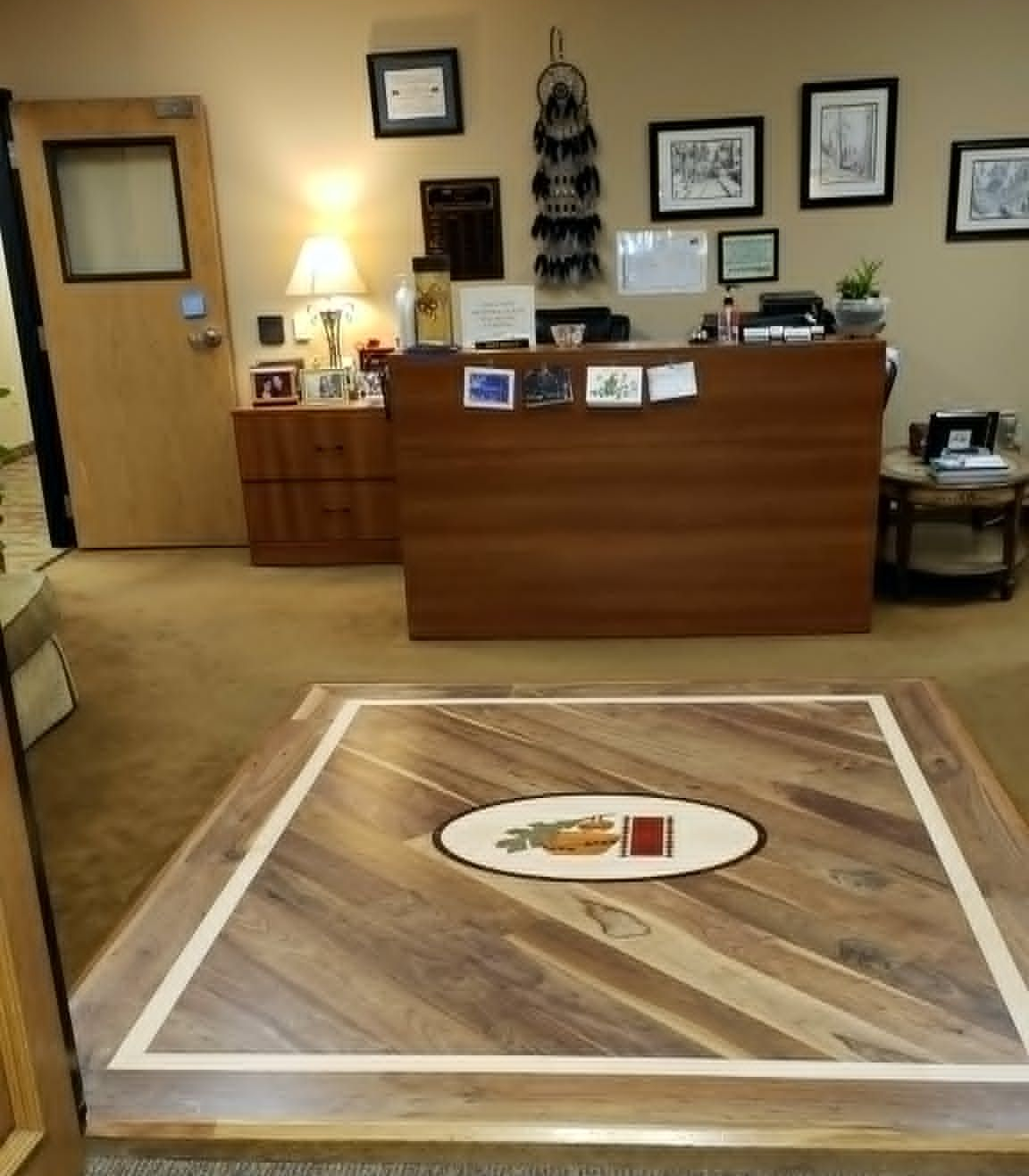 Office reception area with a wooden desk, framed wall art, and a decorative rug in the foreground