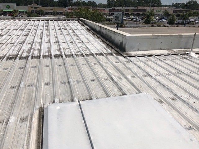 White metal commercial roof with patches and debris, outdoor setting.