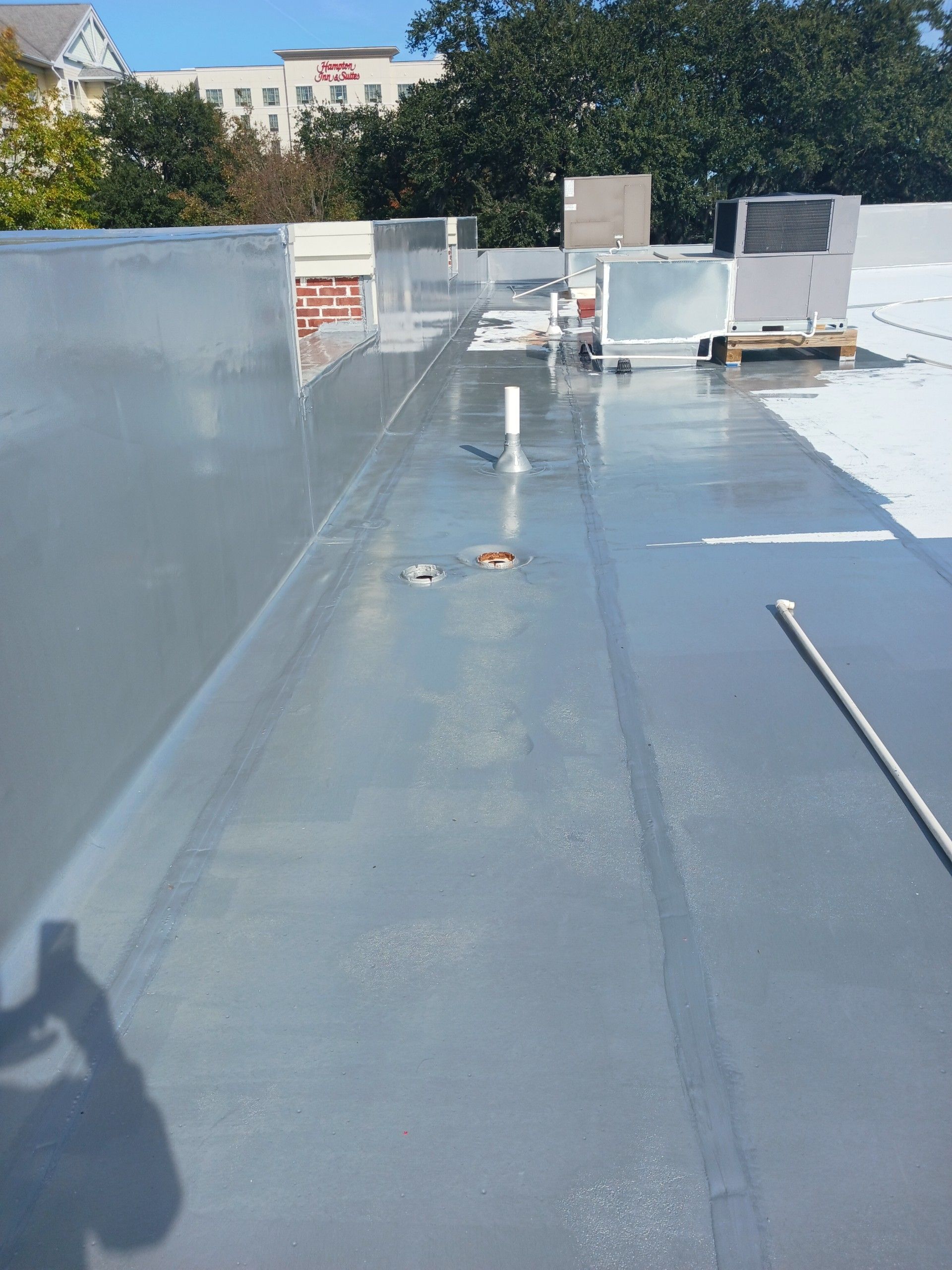 Gray flat roof with equipment and pipes, buildings in background, sunny day.