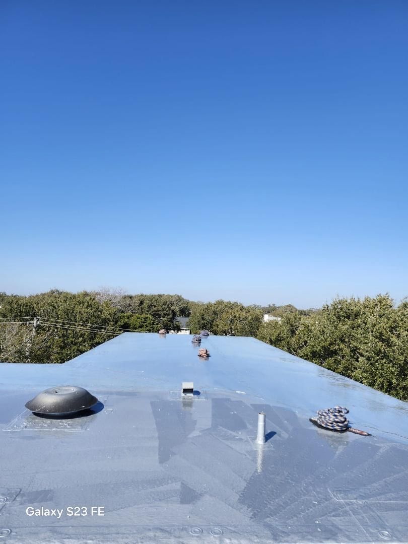 Shiny metal roof reflecting the blue sky, with trees in the background.