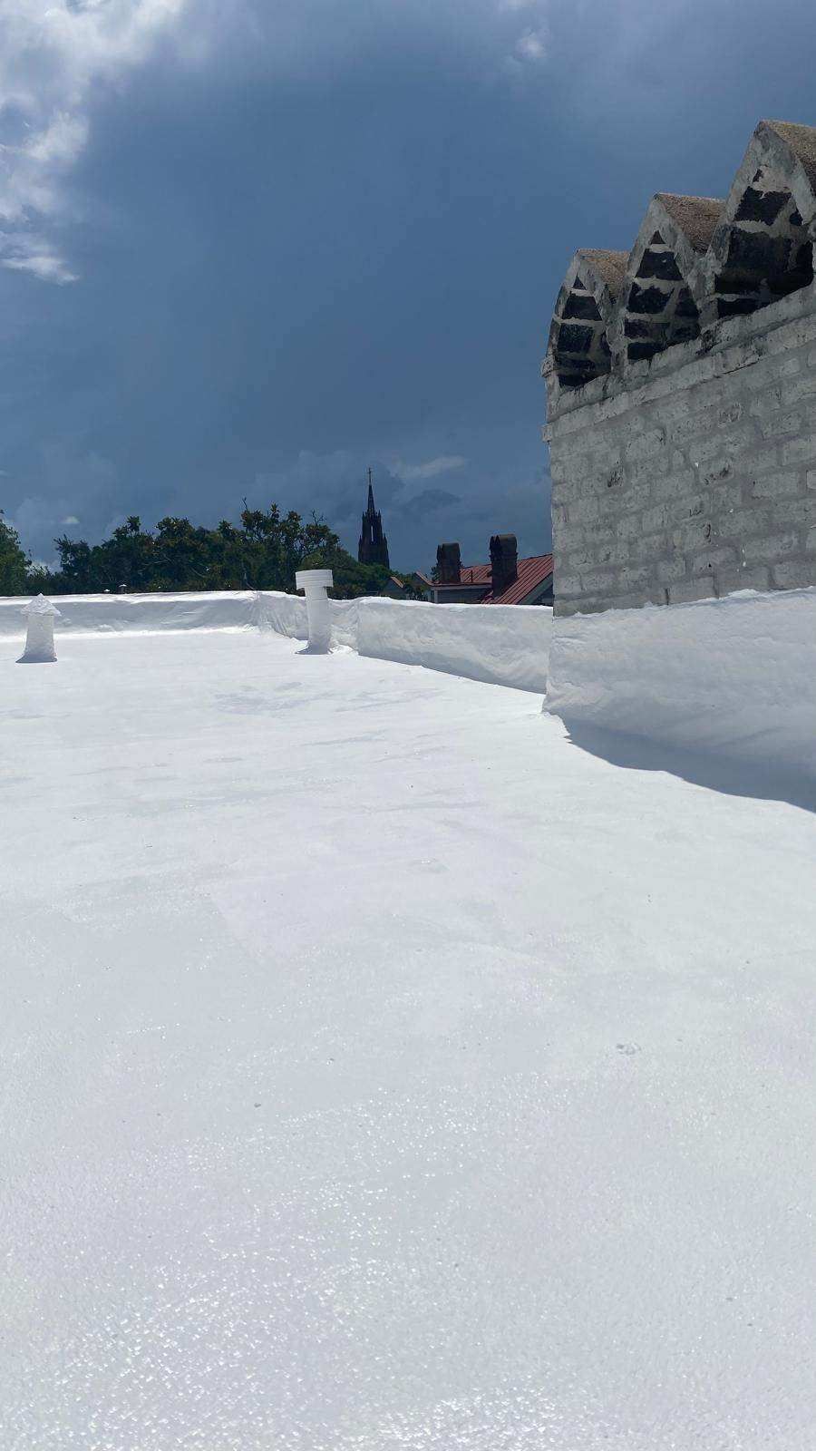 White-coated flat roof on a building, cloudy sky, distant city buildings and a tower visible.