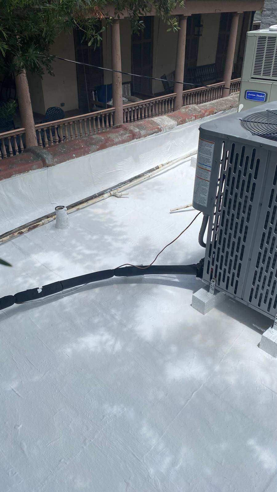 Air conditioning unit on a white roof, black tubing running across the surface, in front of a building.