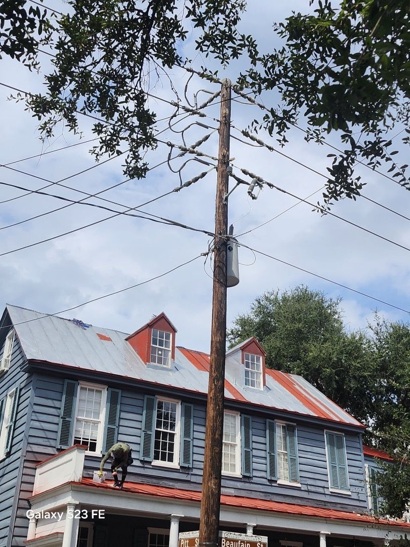 Blue house with red roof, framed by tree branches and power lines against a blue sky.