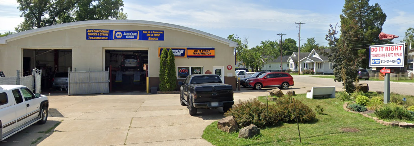 Small auto repair shop with parked vehicles and a sign by the road
