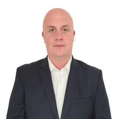 A bald person wearing a dark navy blazer and a crisp white collared shirt against a plain white background.