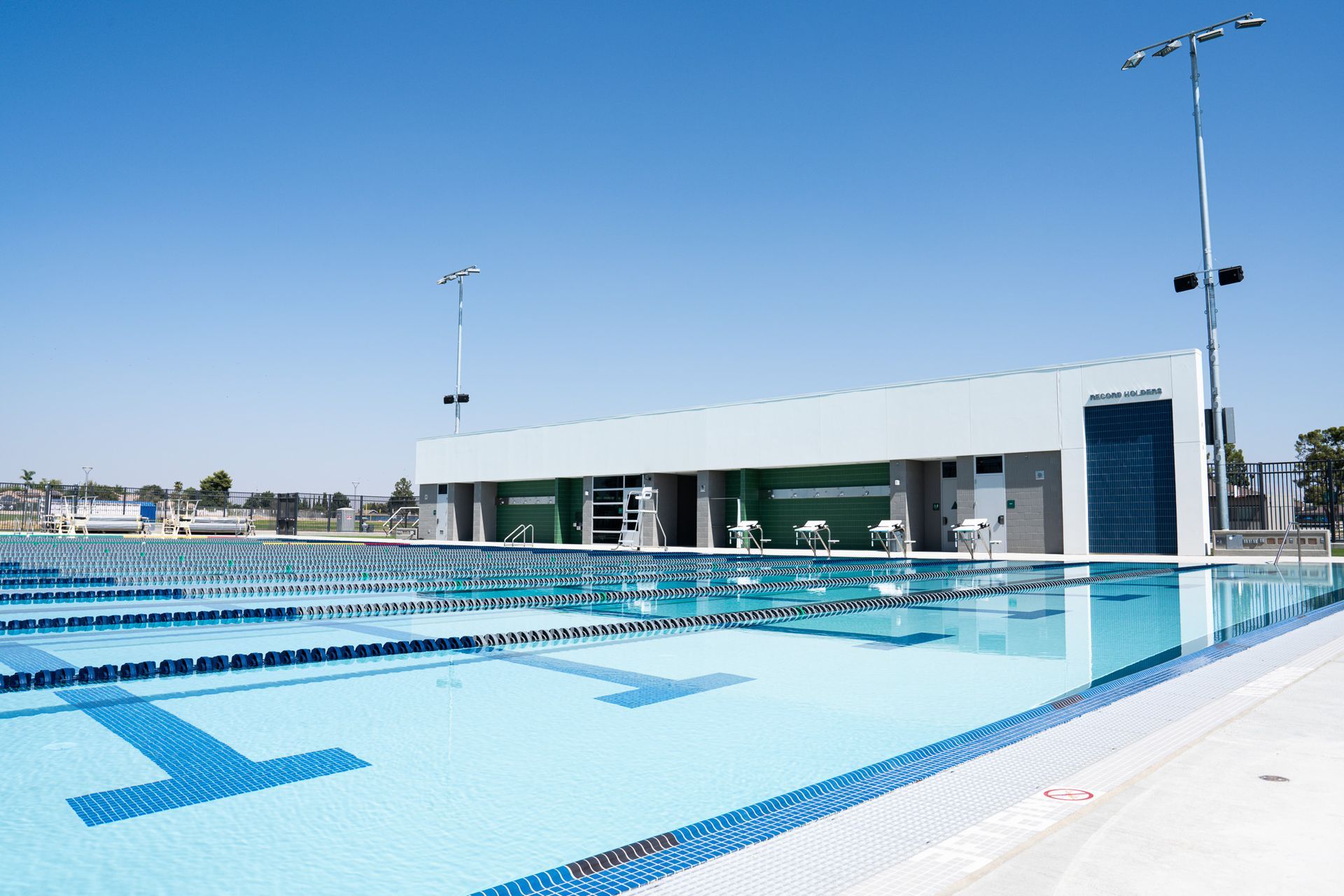Pool with lane markers, building with green accents, blue sky.