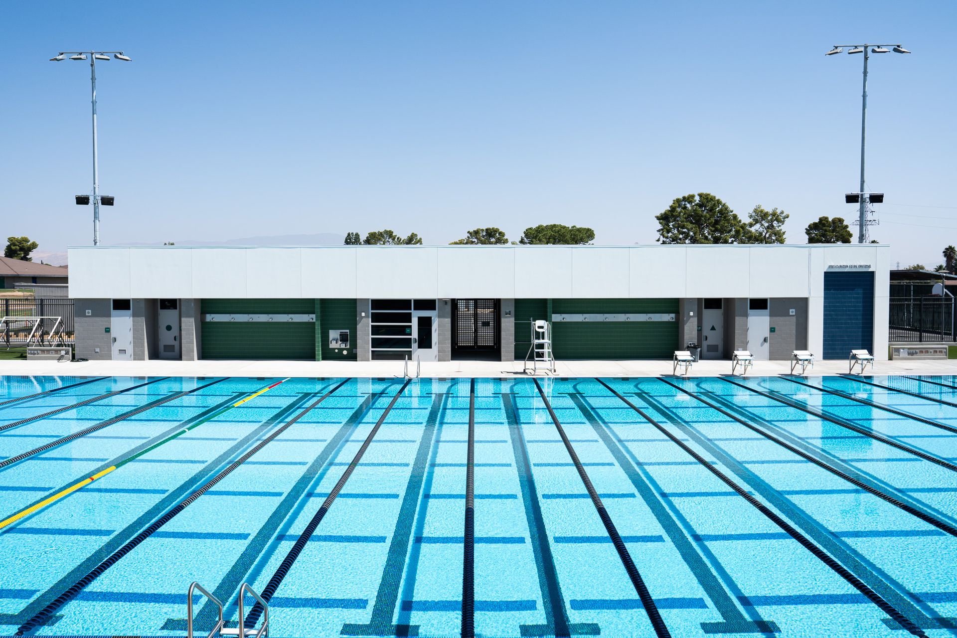 A blue swimming pool with lanes, and a white and green building in the background under a clear sky.