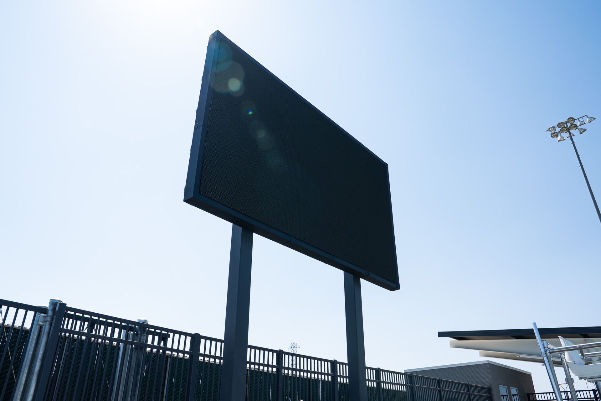 Large blank digital sign, black, on two steel posts outdoors, against a bright blue sky.