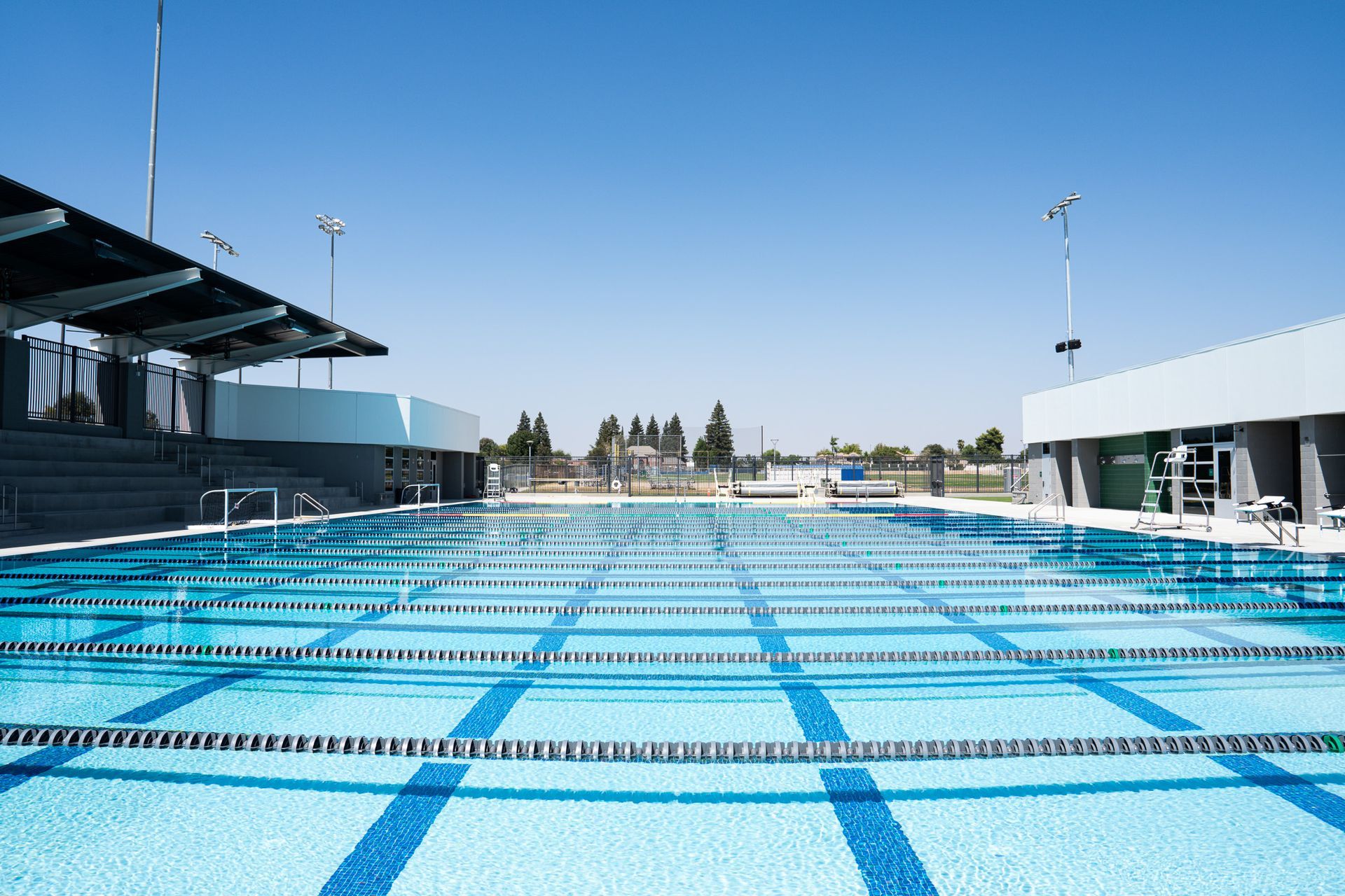 An empty blue swimming pool with lane markers under a clear blue sky.