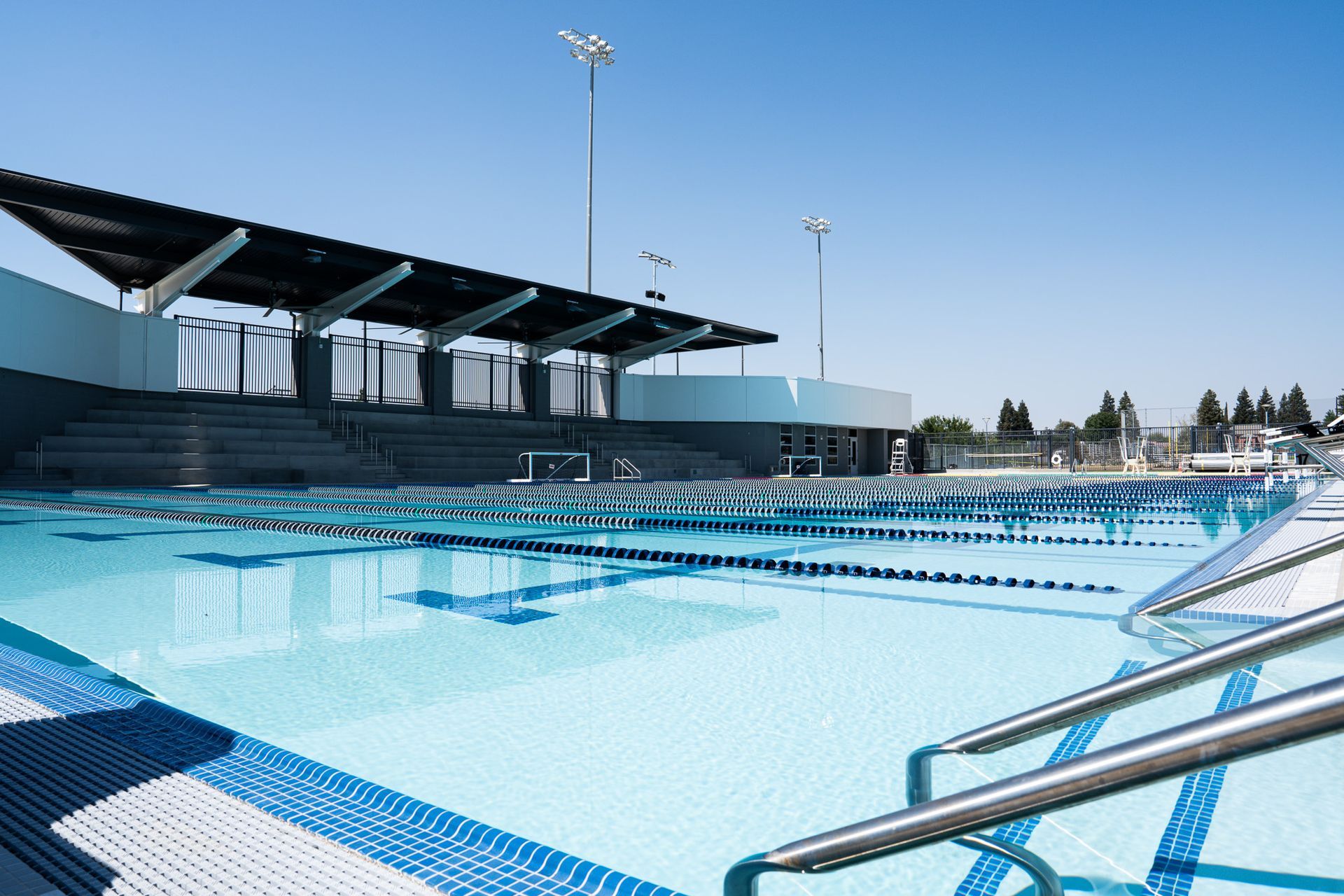 A large outdoor swimming pool with a covered seating area under a bright blue sky.