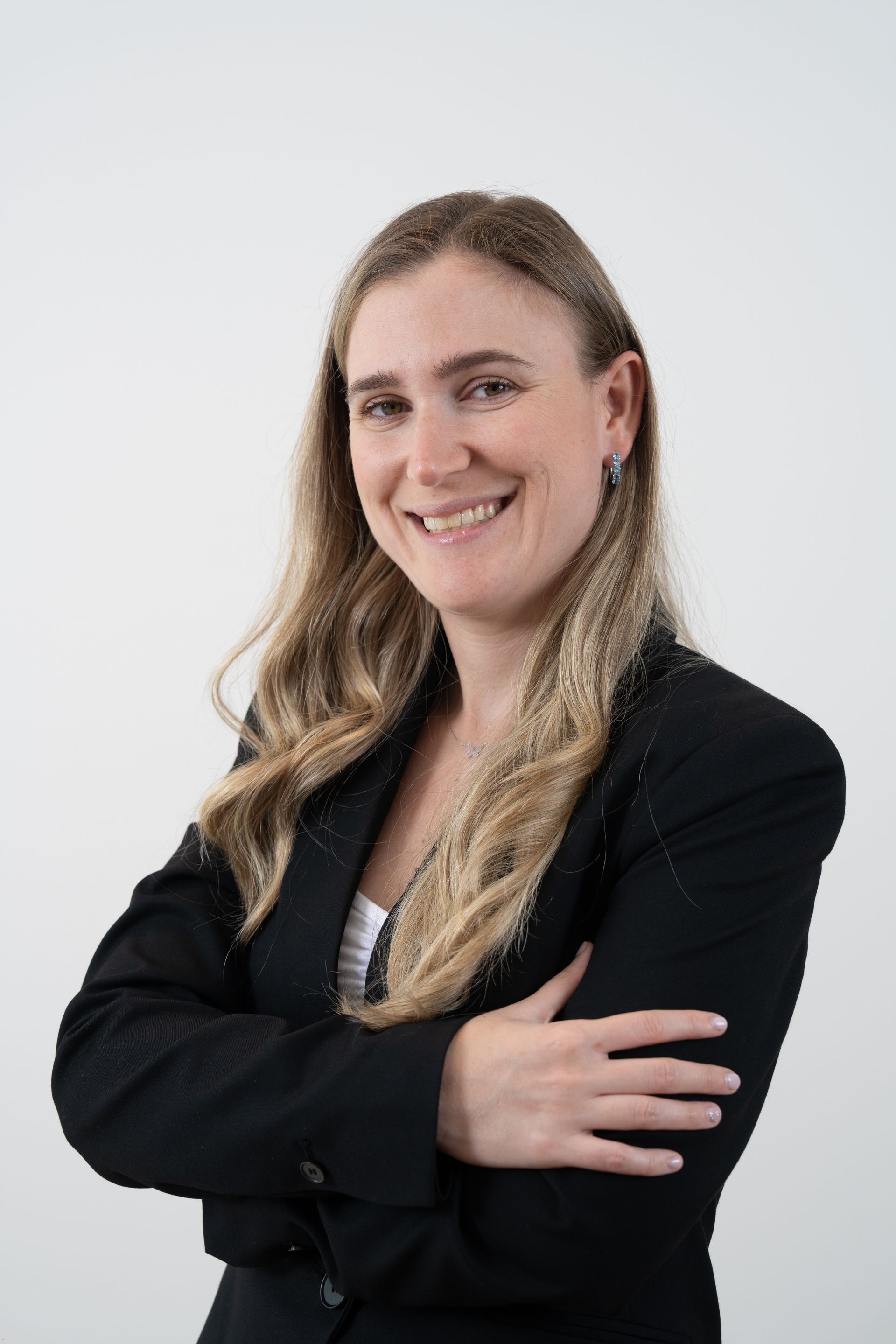 Smiling person in a black blazer with arms crossed against a light background
