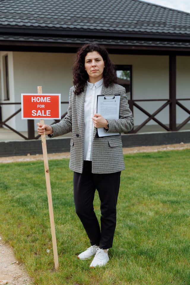 A smiling professional in a pink blazer holds a folder, with a family in the blurred background of a brightly lit room.
