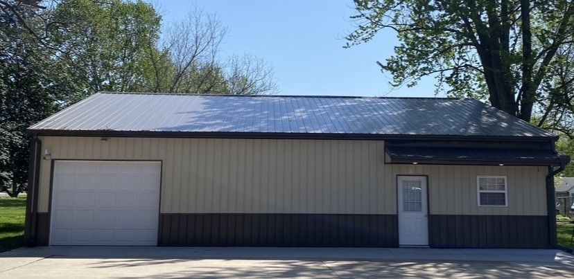 Beige metal-sided building with a garage door, door, and window under a clear, blue sky.