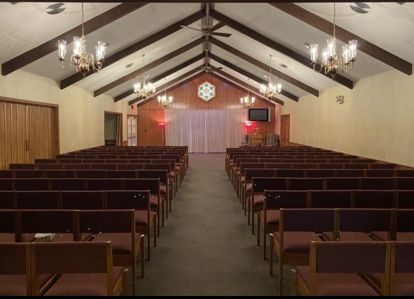 Interior of a funeral home with rows of empty seating facing a raised platform and curtained backdrop.