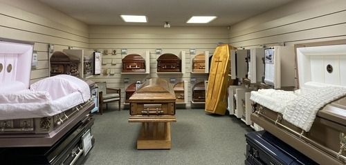 Interior view of a funeral home showroom with various caskets on display, a few elevated on platforms.