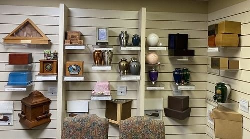 Display of urns of various shapes, sizes, and colors on shelves in a funeral home setting.