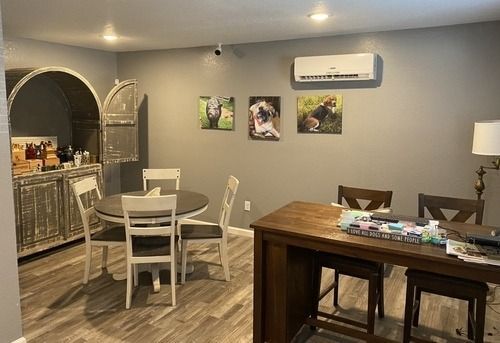 Dining area with a round table, chairs, bar-style table, dog portraits, and a cabinet.