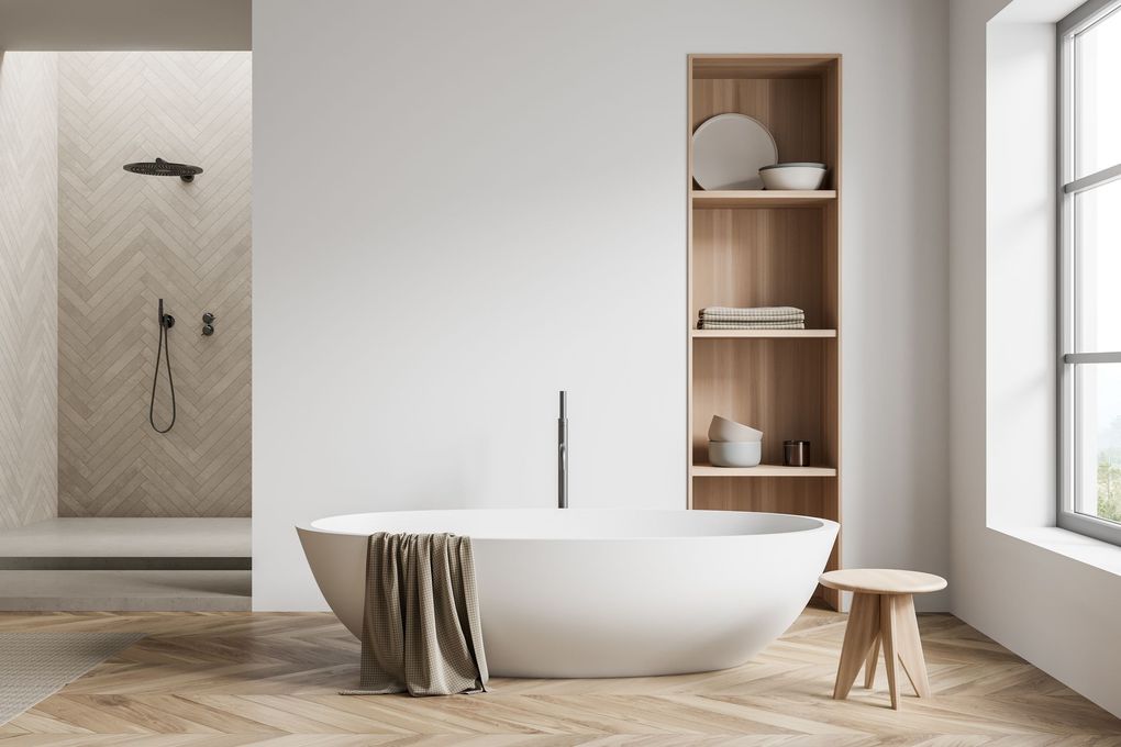 Bagno minimalista con vasca bianca freestanding, dettagli in legno, angolo doccia e mensola accanto alla finestra.