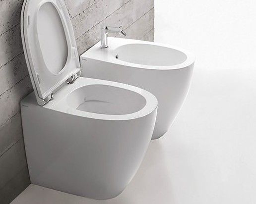 In un bagno luminoso, due moderni WC bianchi: uno con coperchio aperto e l'altro con lavabo bidet.