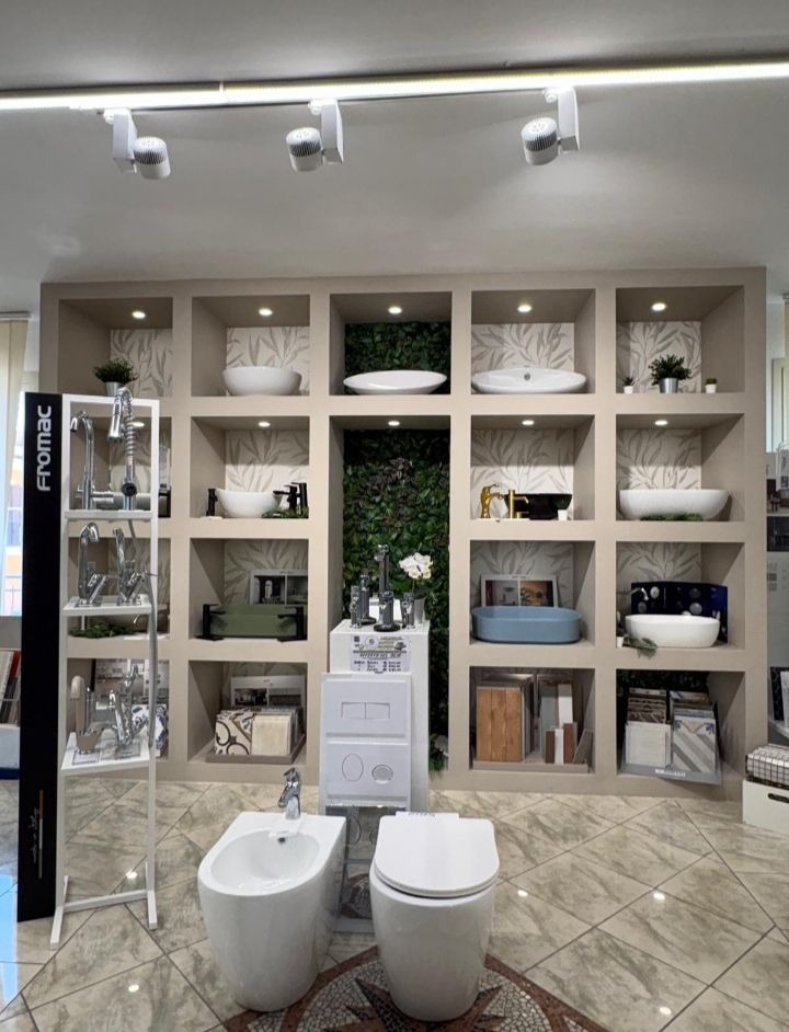 Showroom di bagni con sanitari moderni, lavabo, specchi, piante e pareti piastrellate.