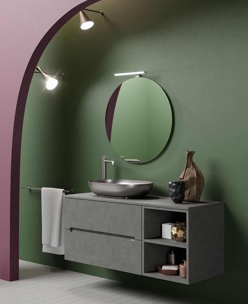 Bagno moderno verde con specchio rotondo, lavabo a ciotola, mobiletto a righe e illuminazione ad arco.