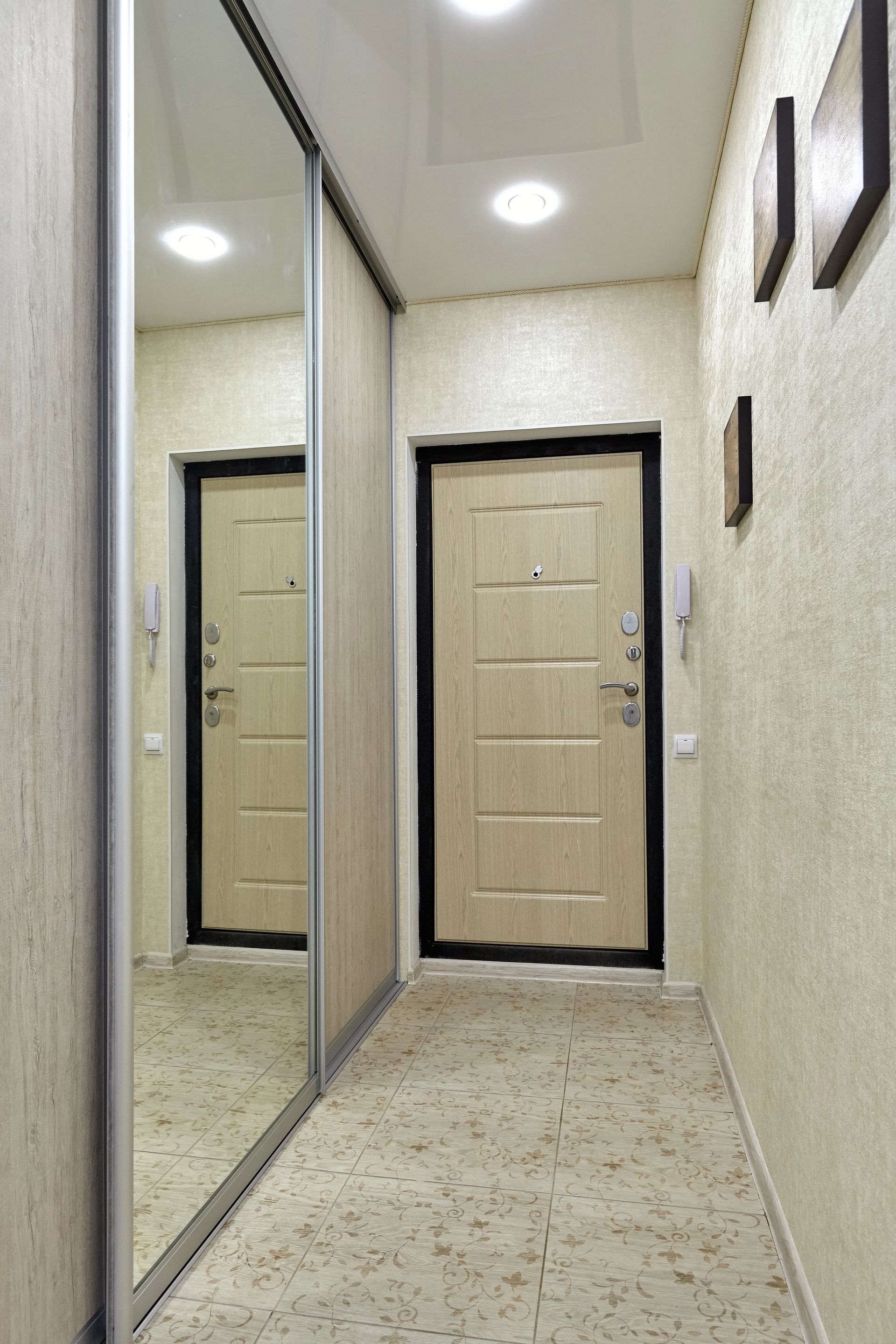 Stretto corridoio con ante dell'armadio a specchio e porta d'ingresso beige in fondo.