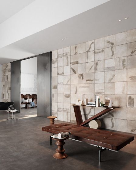 Atrio moderno con parete in pietra, pavimento scuro e panchine scultoree in legno in primo piano.