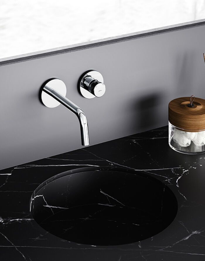 Lavabo moderno con rubinetto cromato e piano in marmo nero.