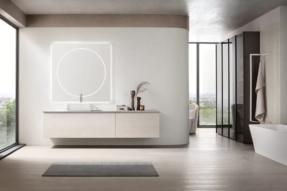Bagno moderno e minimalista con mobile lavabo sospeso, specchio rotondo, cabina doccia e tonalità di grigio.