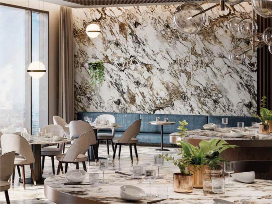 Elegante salotto con parete decorativa in marmo, tavolini rotondi, sedie beige e lampade a sospensione in un interno moderno.
