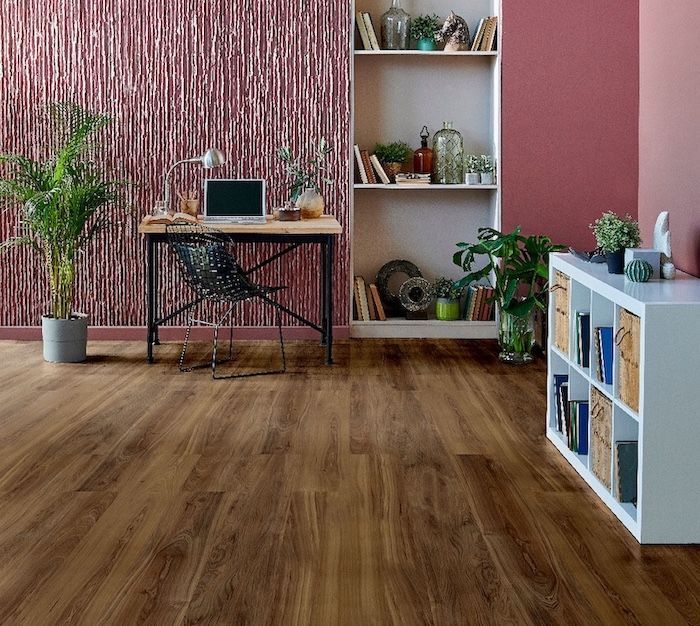 Soggiorno moderno con pavimento in legno, parete rosa con texture, scrivania, mensole, piante e mobile contenitore bianco.