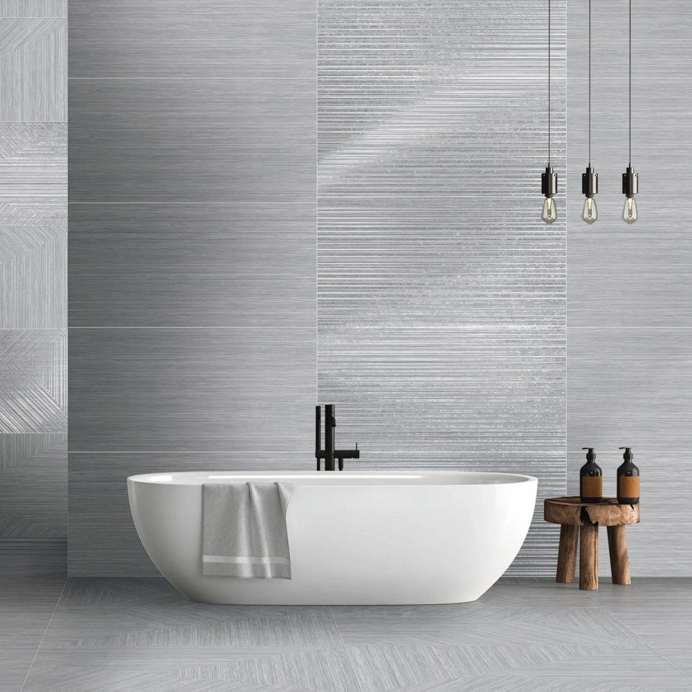 Bagno moderno con vasca freestanding bianca, pareti rivestite con piastrelle grigie, lampade a sospensione e sgabello in legno con articoli da toeletta.
