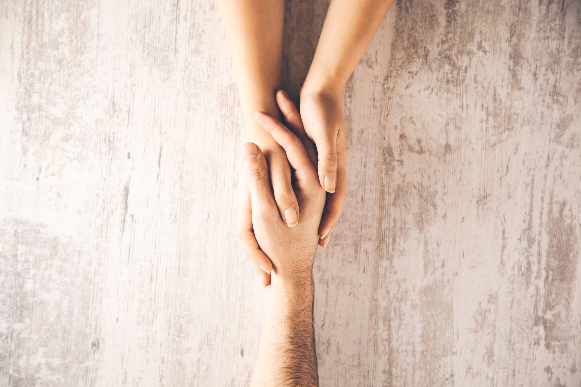 Two hands reaching and holding together against a light textured background