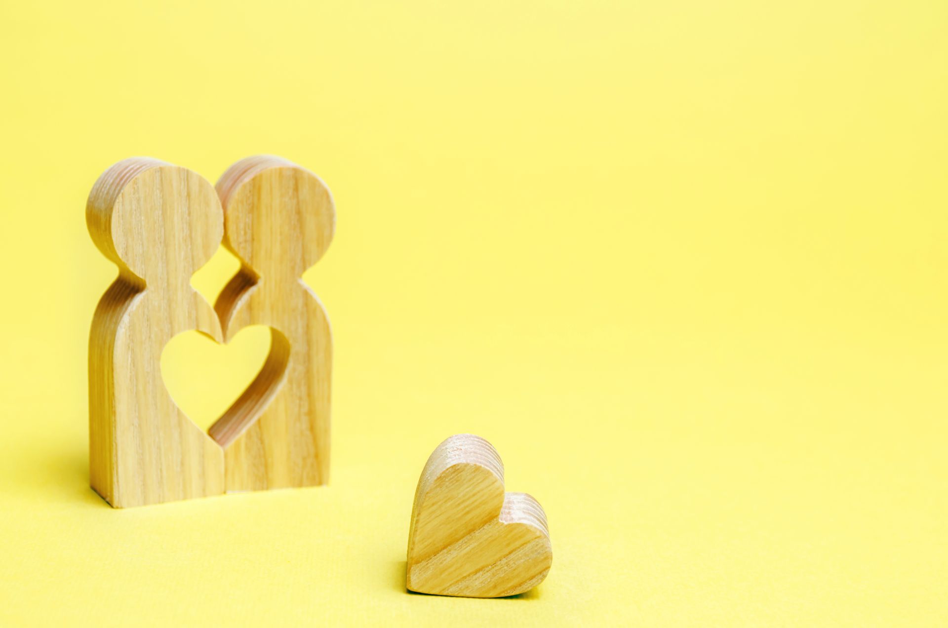 Wooden heart-shaped blocks on a yellow background, with one small heart in the foreground.