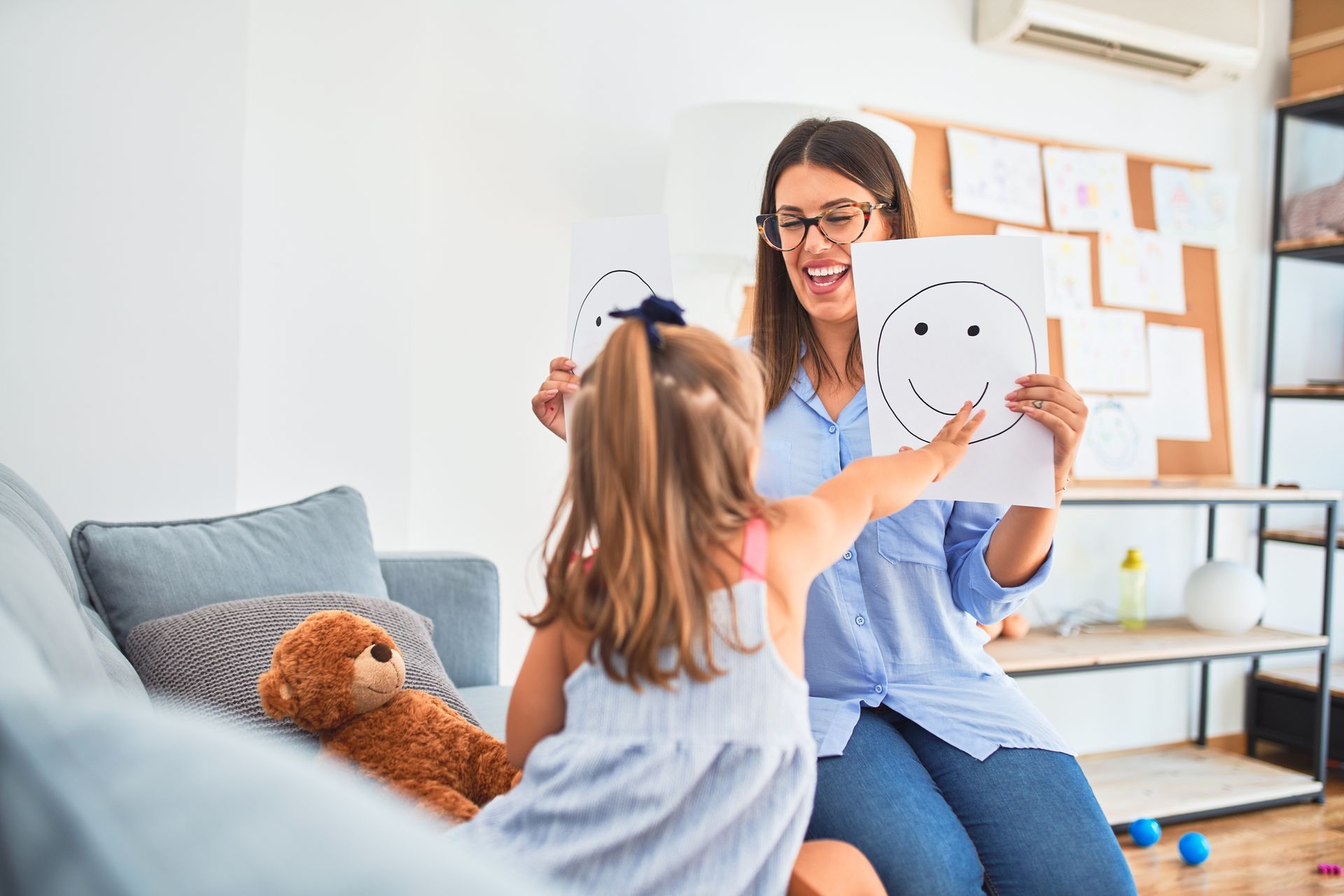 Therapist showing a smiley face drawing to a child in a bright living room