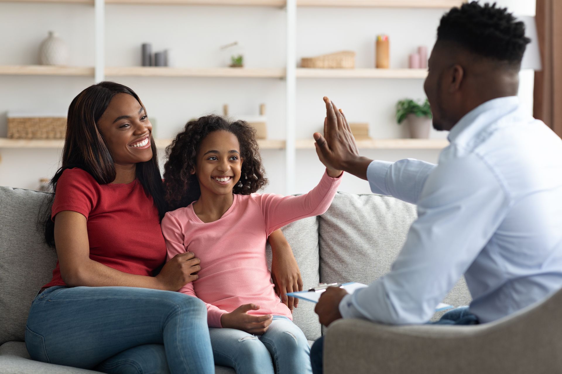 Smiling mother and daughter high-five with child family counselor during a positive session. Smiling mother and daughter high-five with child family counselor during a positive session.