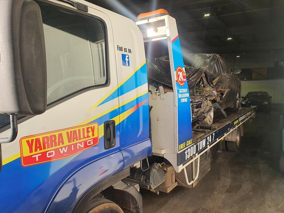 Tow truck with wrecked car on the flatbed in a dimly lit garage.