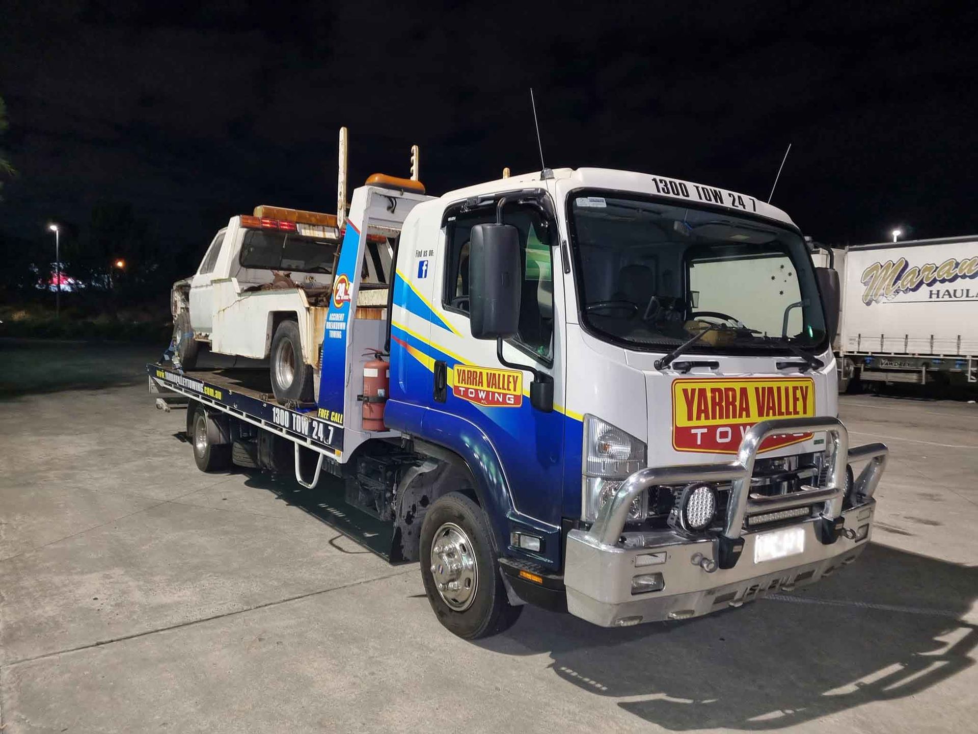 Tow truck with a white vehicle on its flatbed at night.