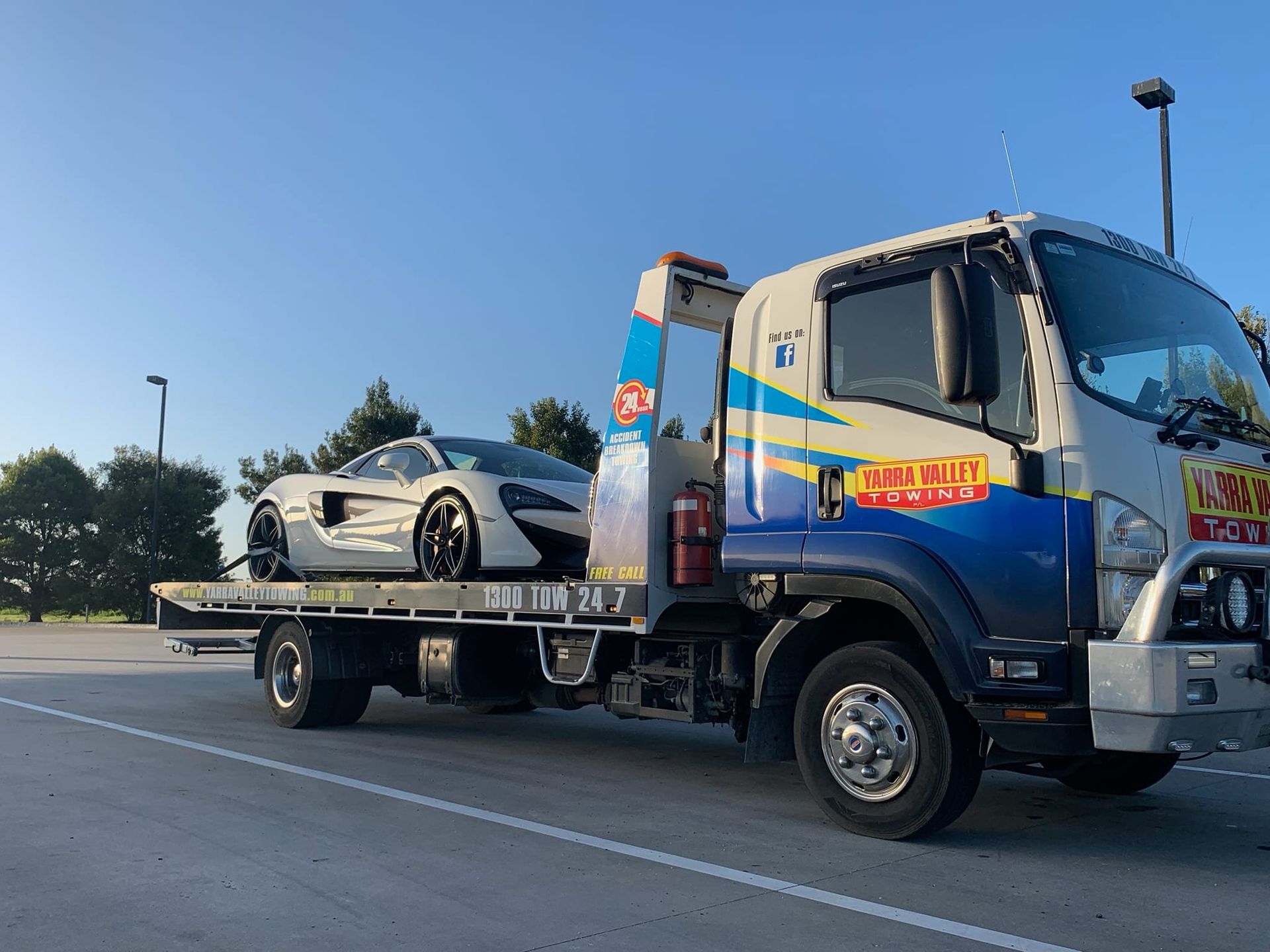 White McLaren sports car on a flatbed tow truck. Clear sky in a parking lot.