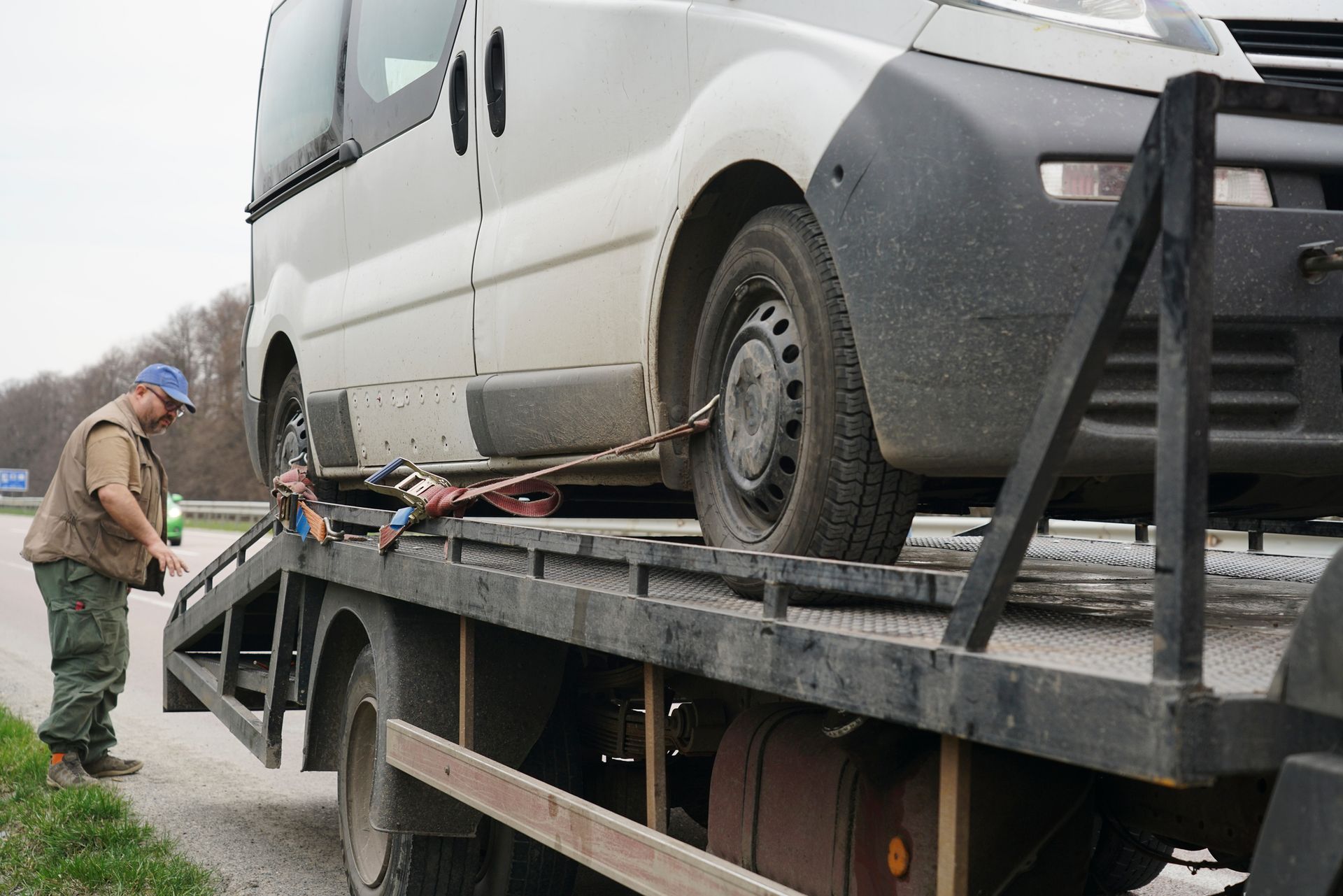 Tow truck loading a white van, man attaching straps on the roadside.