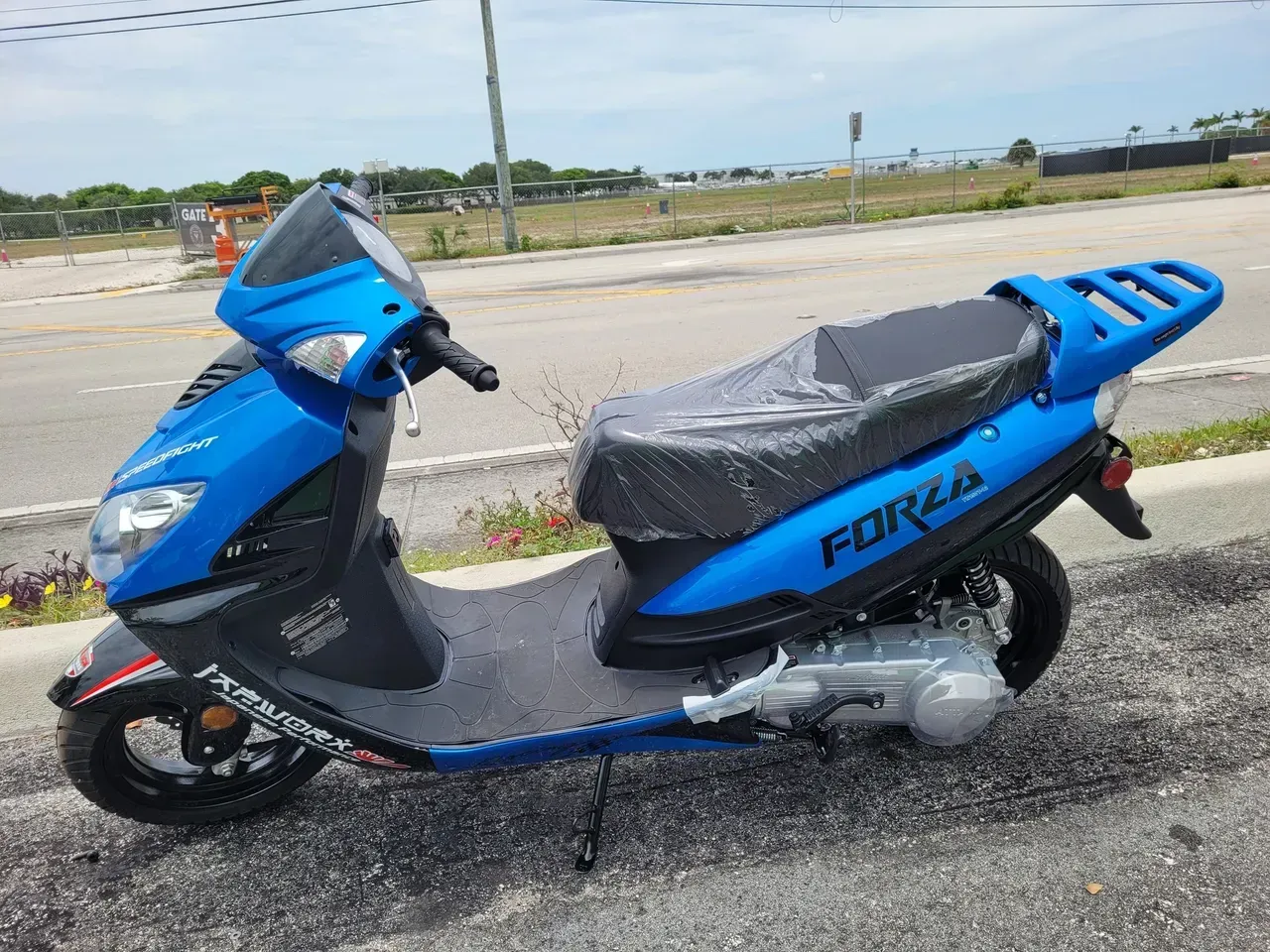 Blue scooter parked on a roadside, covered seat, with a coastal background