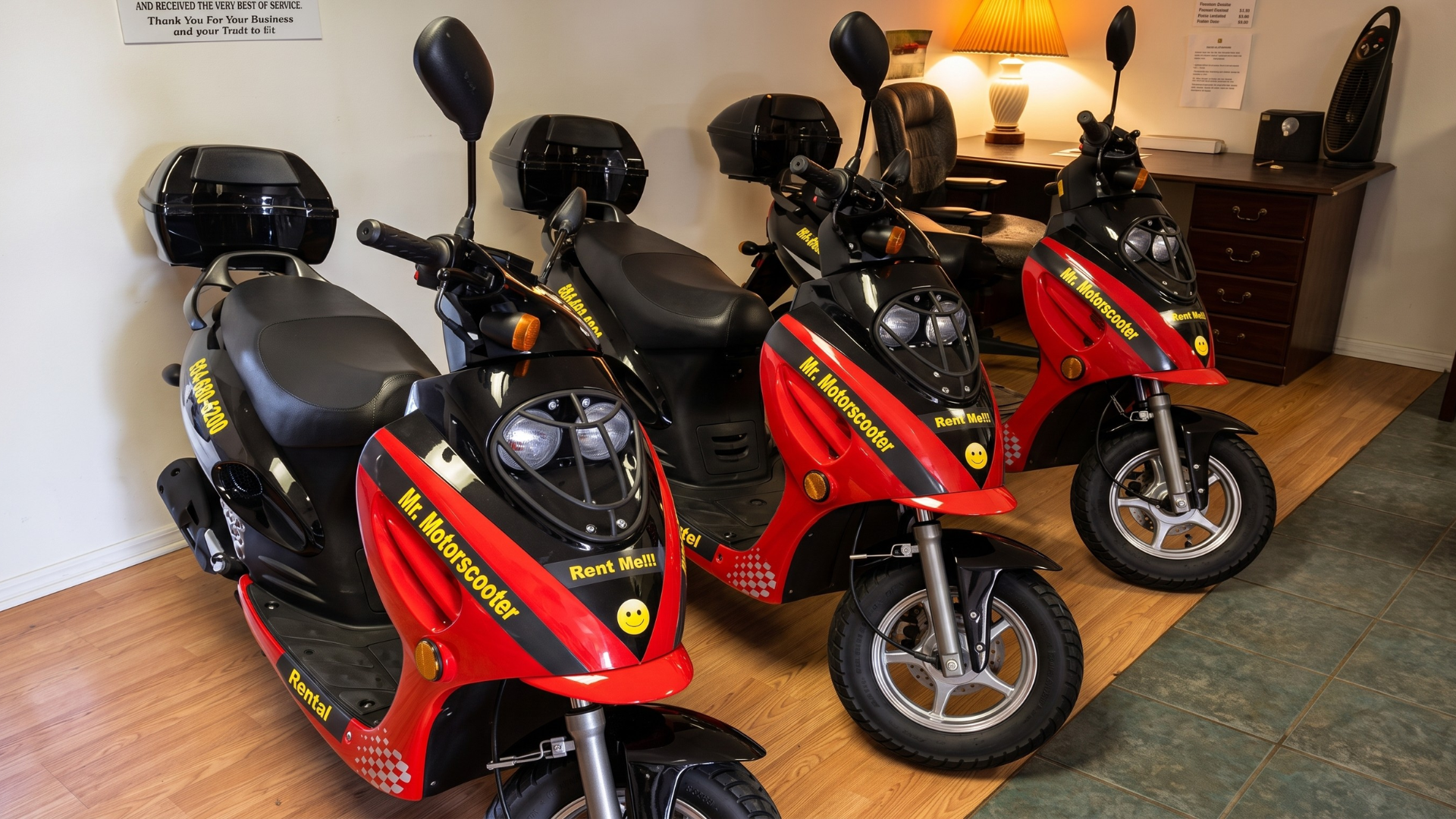 Three red-and-black scooters parked indoors on a wooden floor.