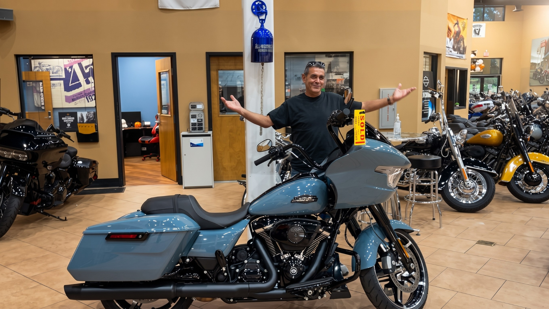 Man in a motorcycle showroom posing behind a blue touring bike, with other motorcycles in the background
