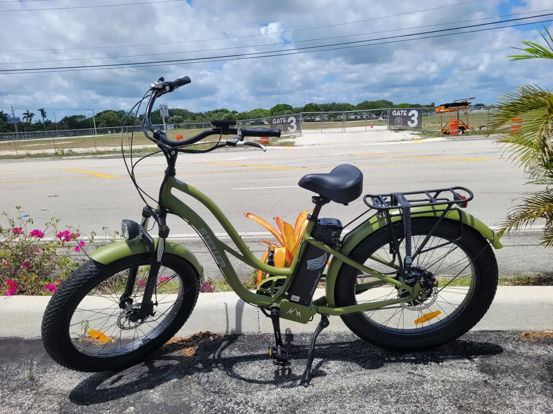 Green electric bike parked beside a beach with ocean and cloudy sky in the background