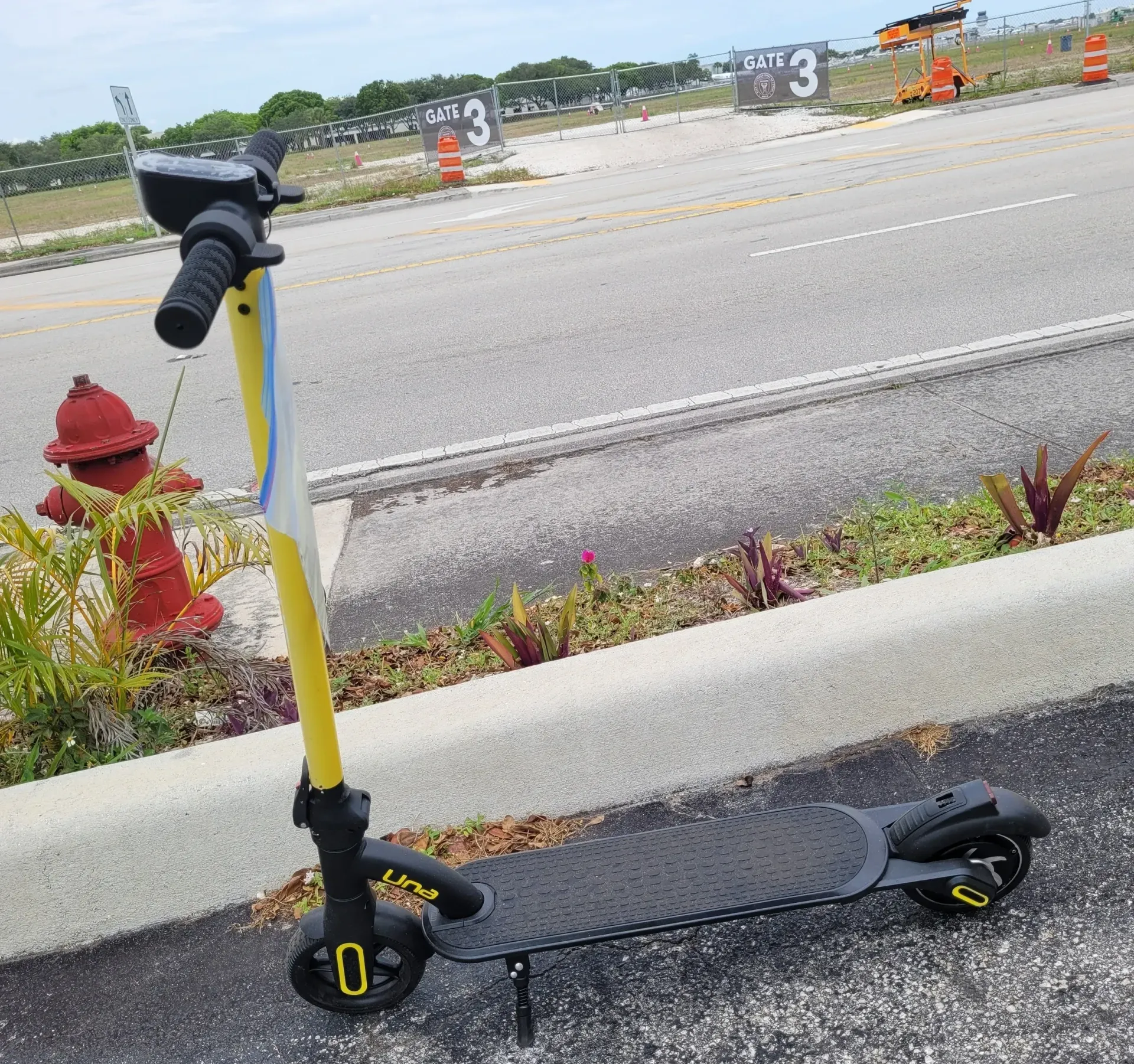 Black-and-yellow electric scooter parked beside a curb near a red fire hydrant on an empty street