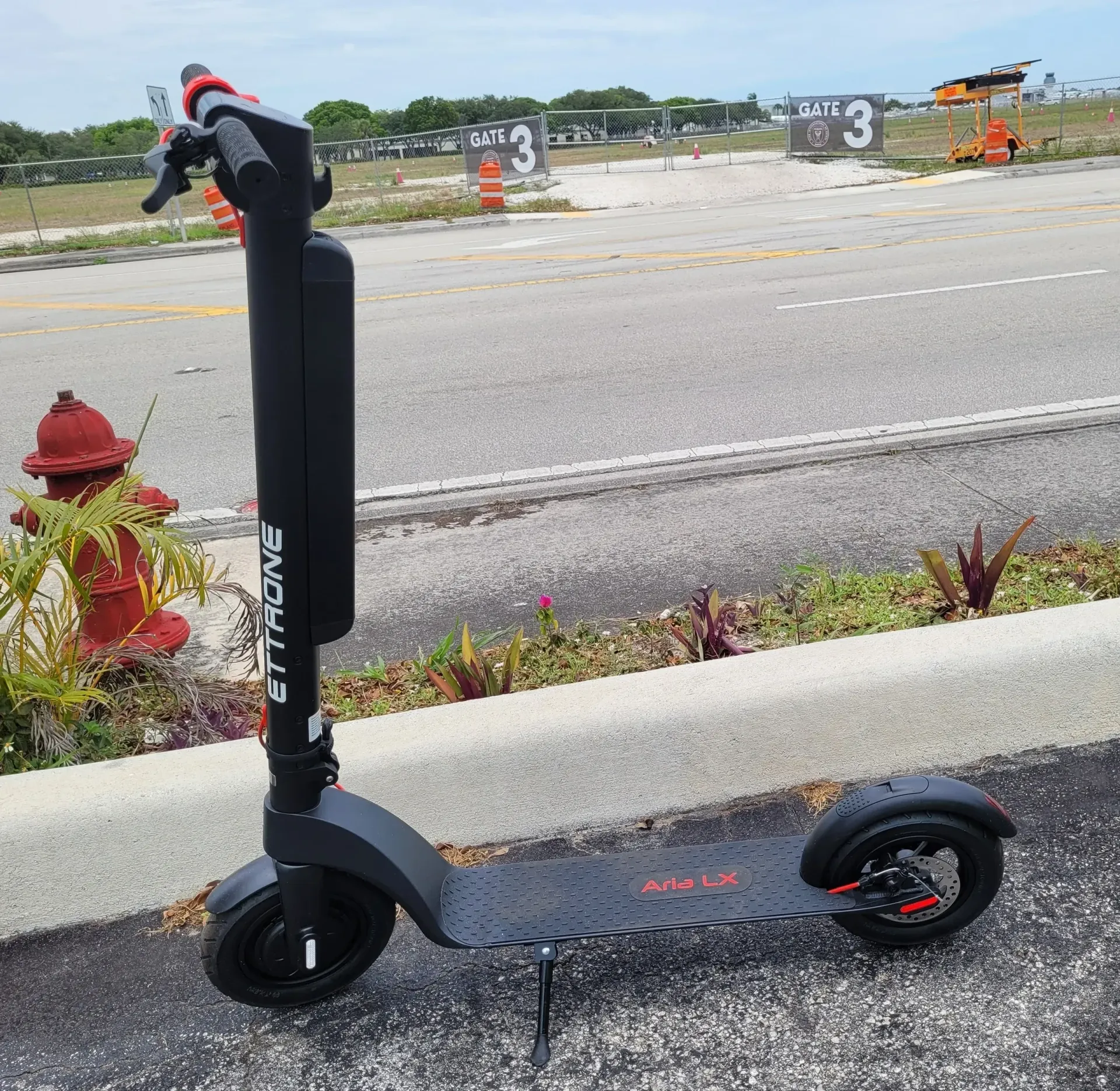 Black electric scooter parked by a roadside near a red fire hydrant and grassy lot.