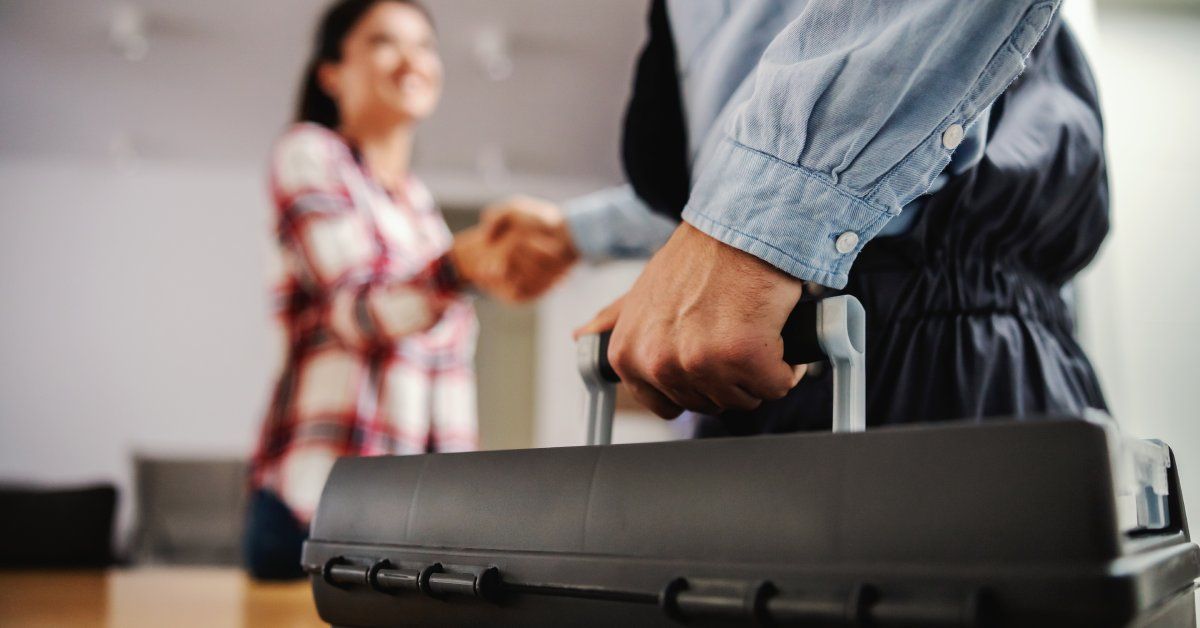 A handyman shakes the hand of a homeowner as they hold a black toolbox to complete a home project.