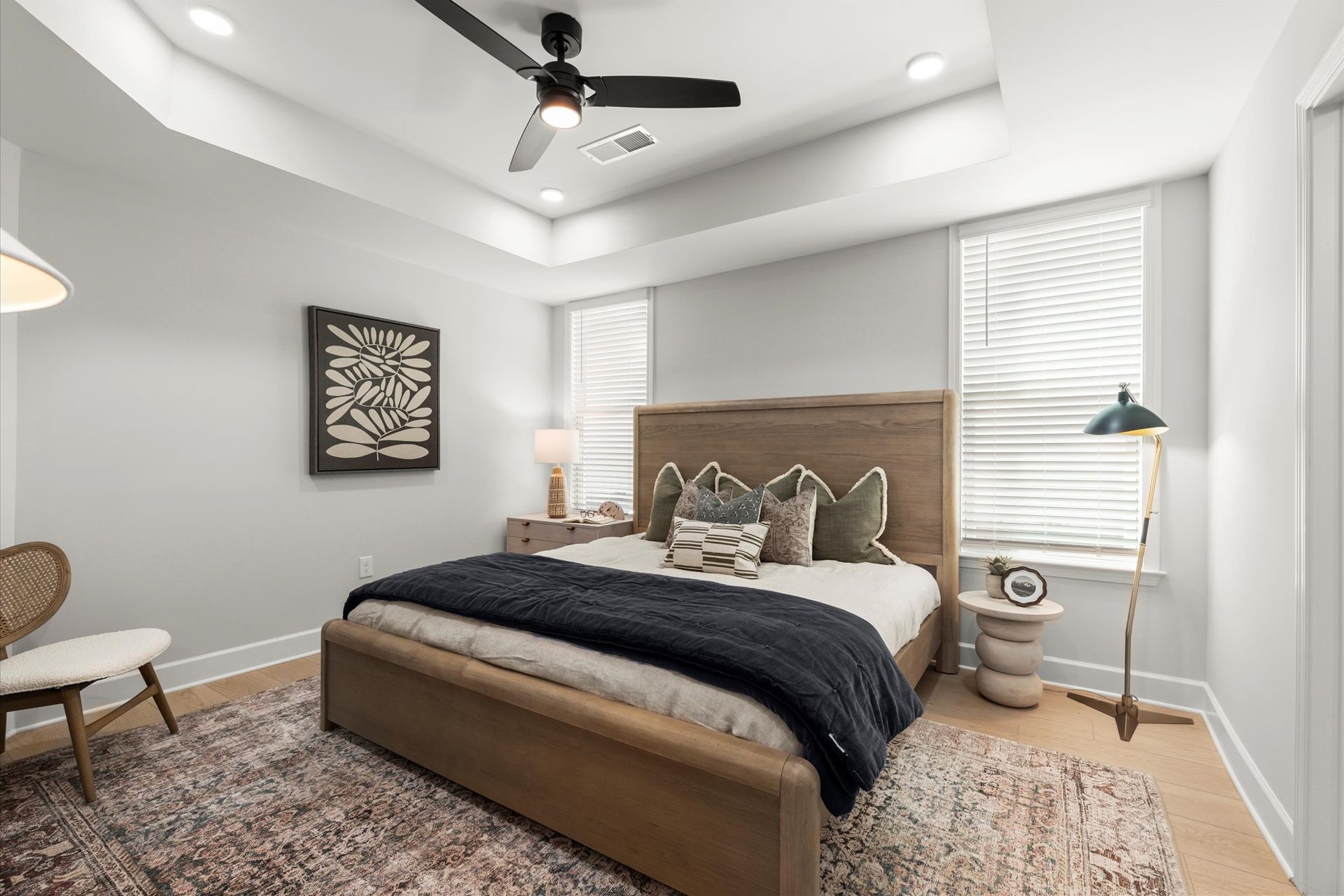 Bedroom with a wooden bed, rug, and artwork. Includes a ceiling fan and a reading chair.