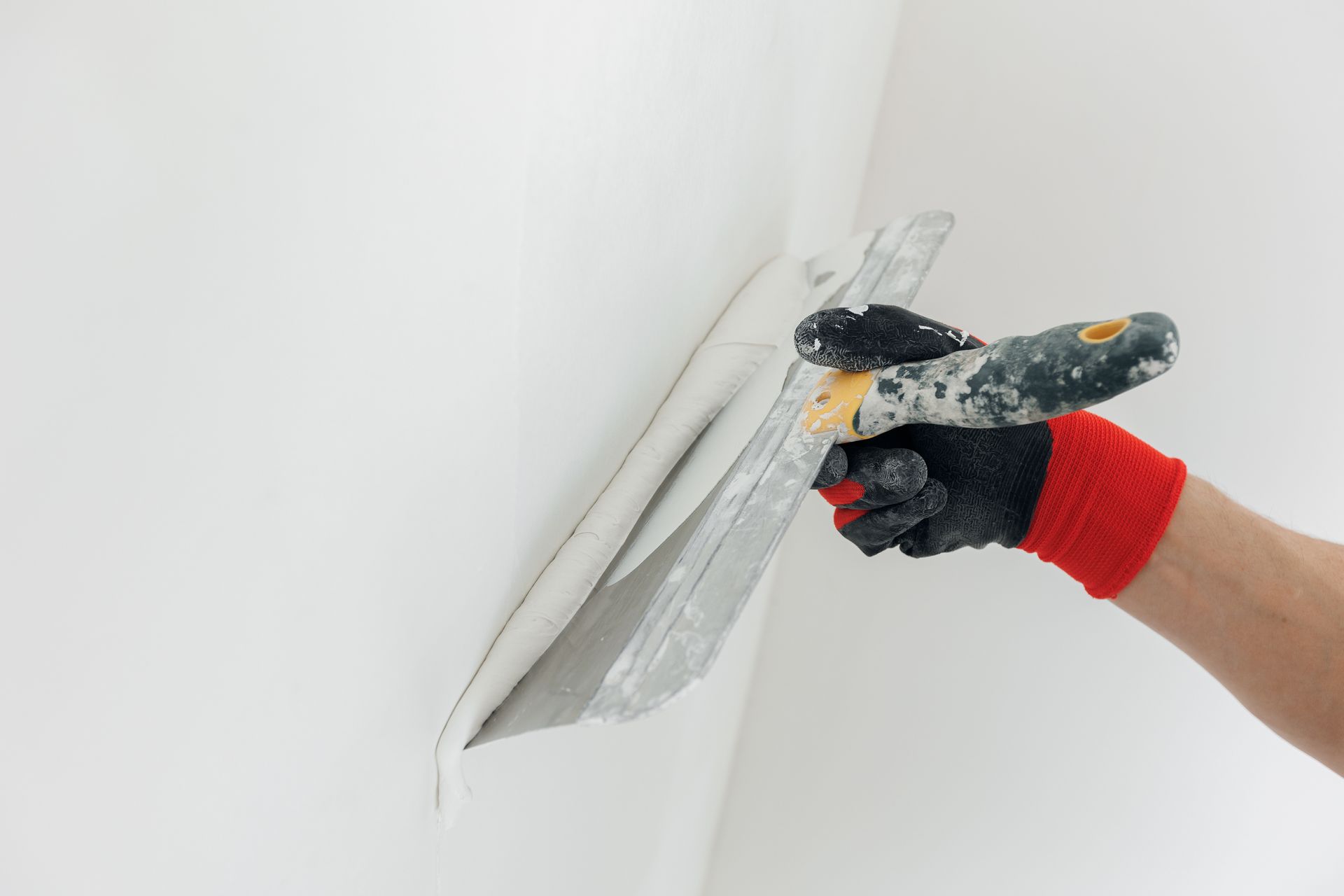 A person in work gloves uses a trowel to apply plaster to a white wall.